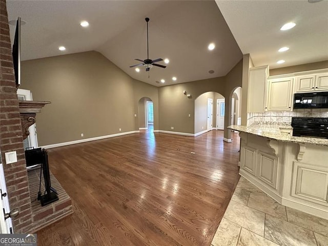 unfurnished living room featuring light hardwood / wood-style floors, lofted ceiling, ceiling fan, and a brick fireplace