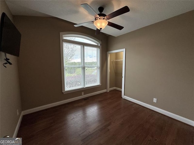 unfurnished bedroom featuring ceiling fan, a closet, dark hardwood / wood-style floors, and a walk in closet