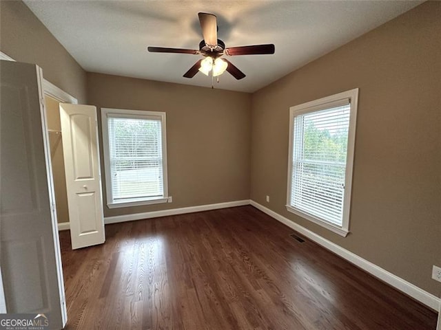 unfurnished bedroom featuring multiple windows, dark hardwood / wood-style floors, and ceiling fan