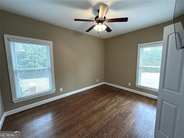 unfurnished room featuring a healthy amount of sunlight, dark hardwood / wood-style flooring, and ceiling fan