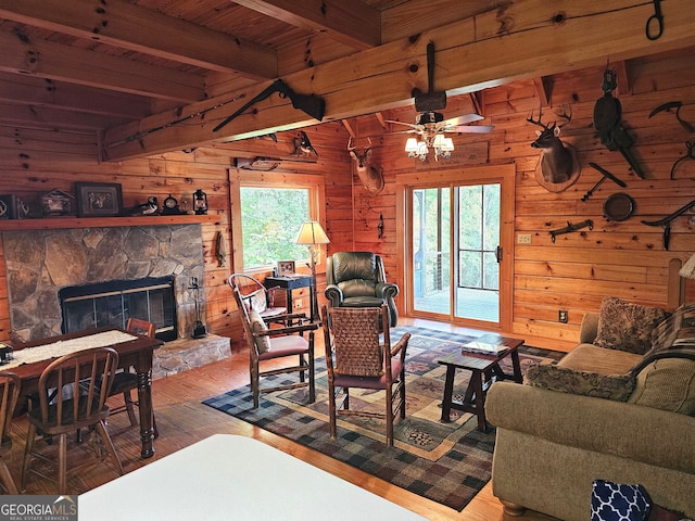 living room featuring wood-type flooring, wooden walls, ceiling fan, beam ceiling, and a fireplace