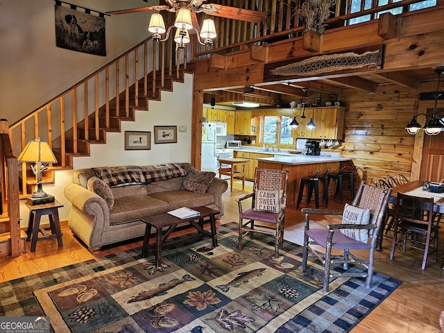 living room featuring hardwood / wood-style flooring, beamed ceiling, a high ceiling, a chandelier, and wooden walls