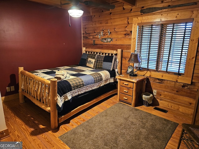 bedroom featuring hardwood / wood-style flooring, wooden walls, and beam ceiling