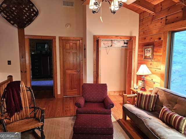 living room with wood-type flooring, beam ceiling, high vaulted ceiling, wood walls, and a chandelier