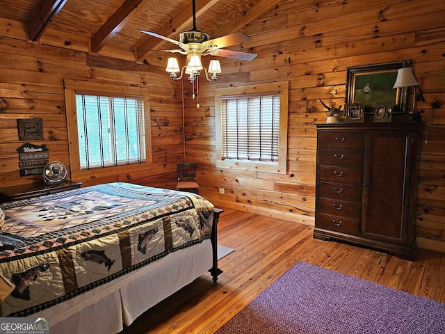 bedroom with light hardwood / wood-style floors, beamed ceiling, multiple windows, and wooden walls