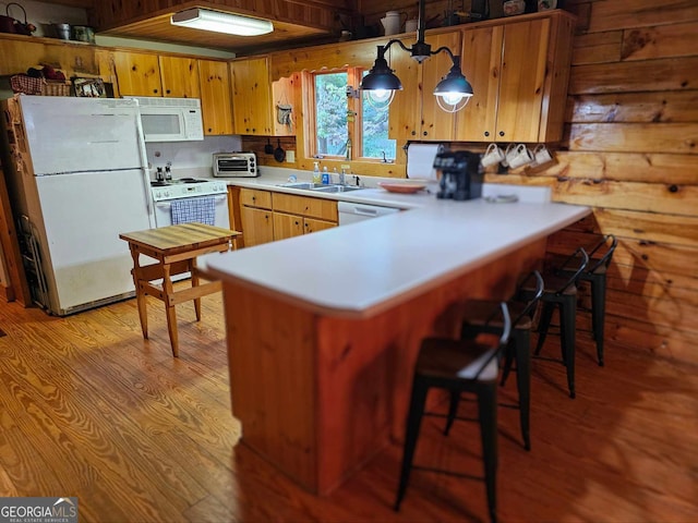 kitchen featuring kitchen peninsula, hanging light fixtures, wooden walls, light hardwood / wood-style flooring, and white appliances