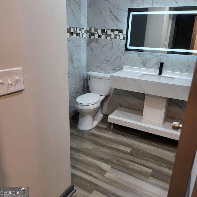 bathroom with wood-type flooring, tile walls, and toilet