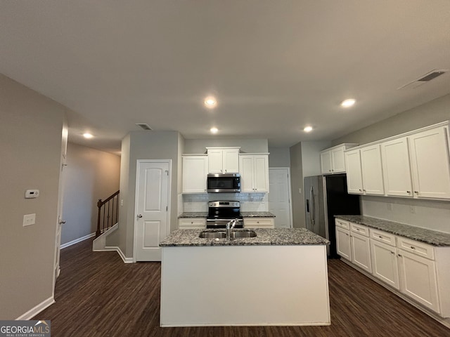 kitchen with an island with sink, dark wood-type flooring, white cabinetry, appliances with stainless steel finishes, and dark stone countertops