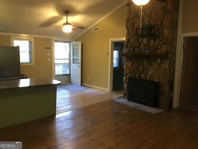 unfurnished living room with a textured ceiling, ceiling fan, light hardwood / wood-style floors, a stone fireplace, and lofted ceiling