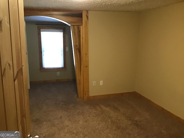 spare room featuring dark carpet and a textured ceiling