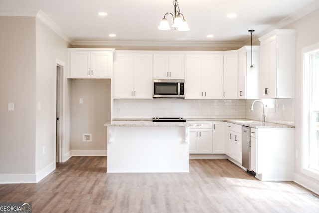 kitchen featuring light stone countertops, stainless steel appliances, crown molding, white cabinetry, and hanging light fixtures