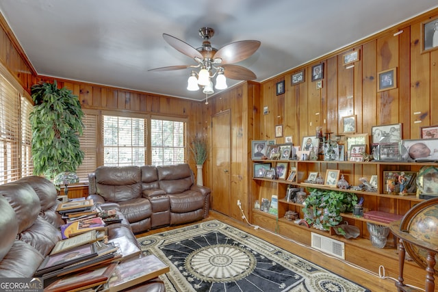 living room with wood-type flooring, wood walls, crown molding, and ceiling fan