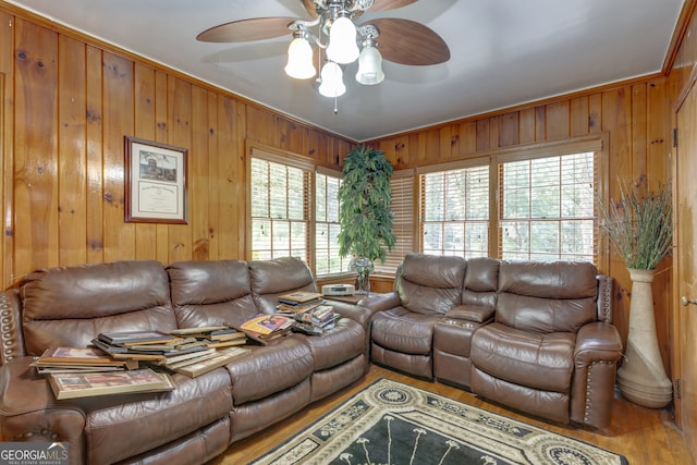 living room featuring wood-type flooring, wood walls, ornamental molding, and ceiling fan