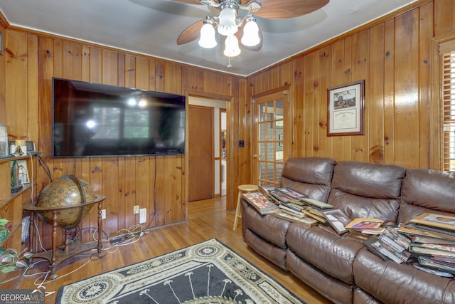 living room with ceiling fan, light hardwood / wood-style flooring, crown molding, and wood walls