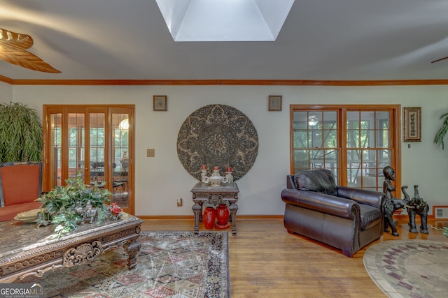 living room with ornamental molding, light hardwood / wood-style floors, a skylight, and ceiling fan