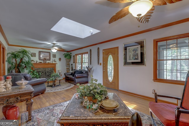 living room with ornamental molding, light wood-type flooring, a skylight, and ceiling fan