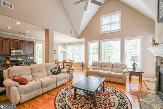 living room featuring high vaulted ceiling, ornamental molding, light hardwood / wood-style flooring, and a fireplace