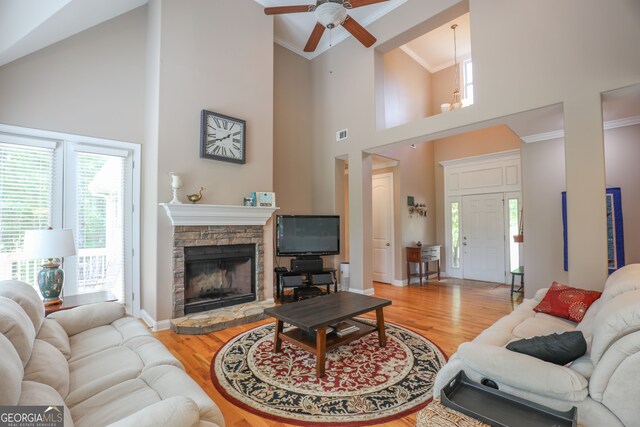 living room featuring light hardwood / wood-style floors, ornamental molding, a stone fireplace, and high vaulted ceiling