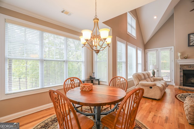 dining space with light hardwood / wood-style floors, a chandelier, a stone fireplace, and vaulted ceiling