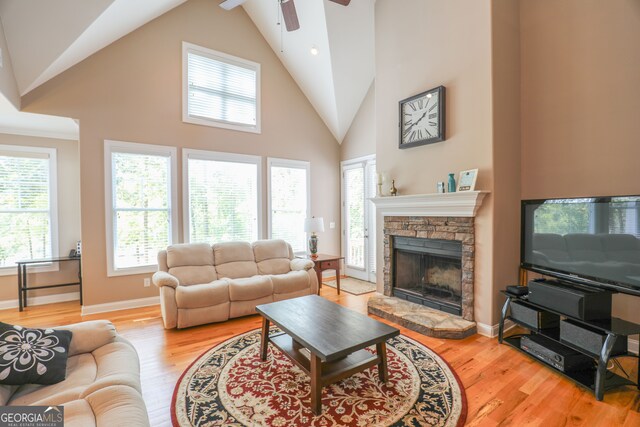 living room featuring a stone fireplace, light hardwood / wood-style flooring, high vaulted ceiling, and ceiling fan