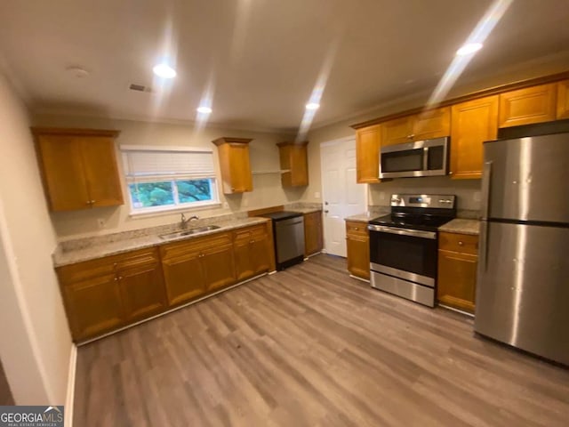 kitchen with light stone countertops, stainless steel appliances, sink, and light hardwood / wood-style flooring