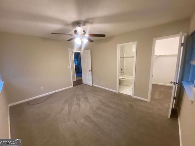 unfurnished bedroom with connected bathroom, dark carpet, a spacious closet, and ceiling fan