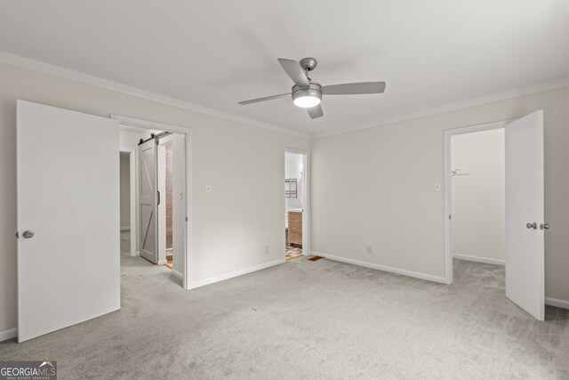 unfurnished bedroom featuring ceiling fan, a barn door, a spacious closet, light carpet, and ensuite bathroom