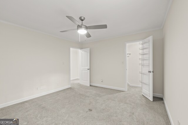 unfurnished bedroom with a closet, ornamental molding, light carpet, a spacious closet, and ceiling fan