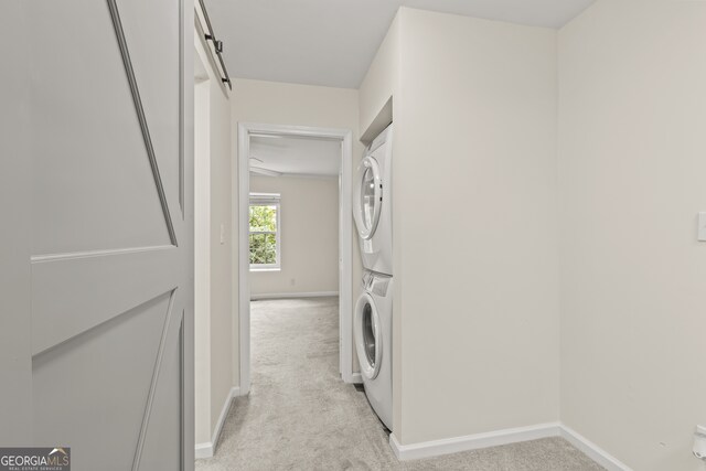 laundry area featuring stacked washer / dryer, a barn door, and light carpet