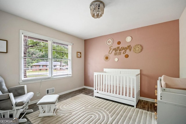 bedroom with dark hardwood / wood-style floors and a nursery area