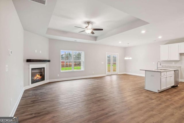 unfurnished living room featuring ceiling fan with notable chandelier, sink, a raised ceiling, and hardwood / wood-style floors