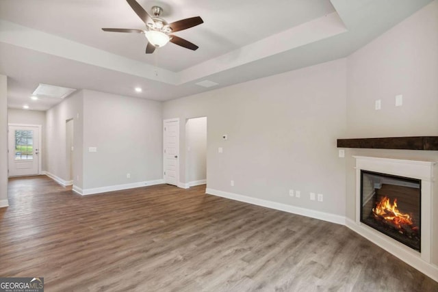 unfurnished living room featuring ceiling fan, hardwood / wood-style flooring, and a raised ceiling