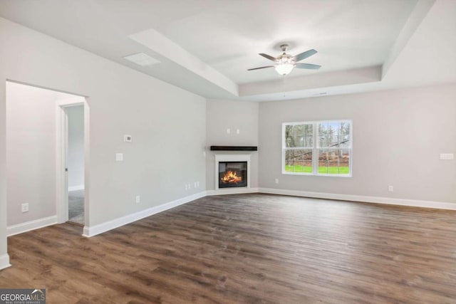 unfurnished living room featuring ceiling fan, a tray ceiling, and dark wood-type flooring