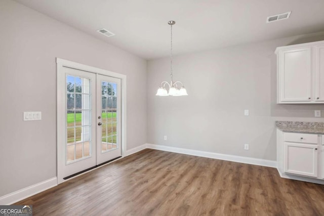 unfurnished dining area featuring an inviting chandelier, hardwood / wood-style floors, and french doors