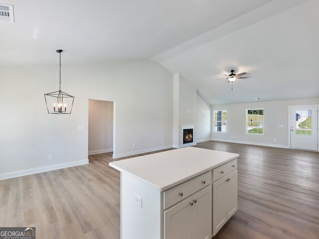 kitchen featuring a center island, lofted ceiling, ceiling fan with notable chandelier, light wood-type flooring, and white cabinetry