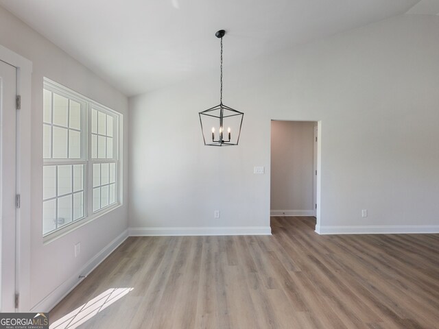 unfurnished dining area with light hardwood / wood-style floors, lofted ceiling, and a notable chandelier