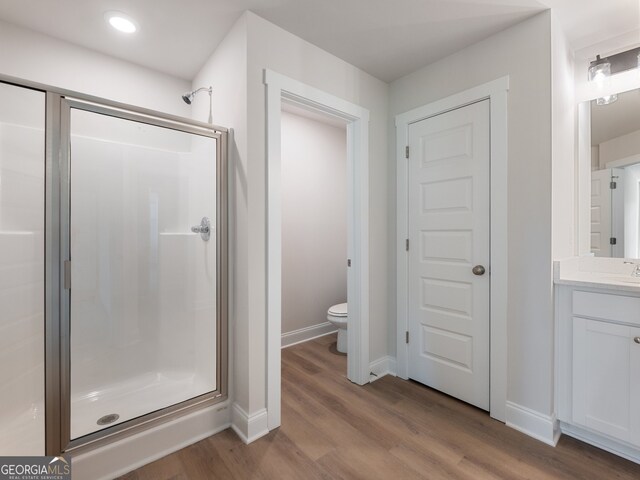 bathroom featuring wood-type flooring, vanity, toilet, and a shower with door