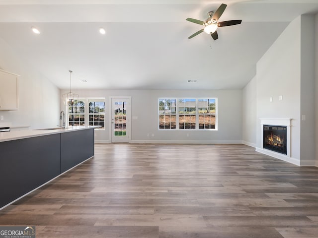 unfurnished living room featuring dark hardwood / wood-style floors, sink, lofted ceiling, and ceiling fan with notable chandelier