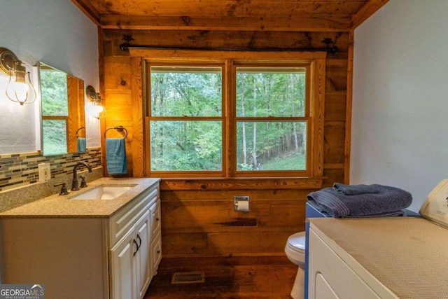 bathroom with vanity, wooden walls, backsplash, and toilet