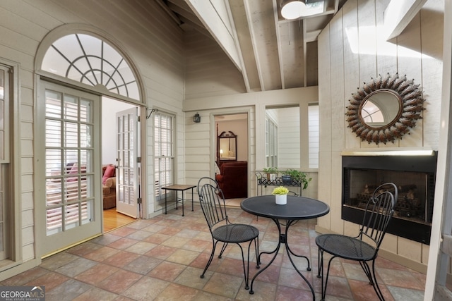 dining area with french doors, beam ceiling, wood walls, and a high ceiling