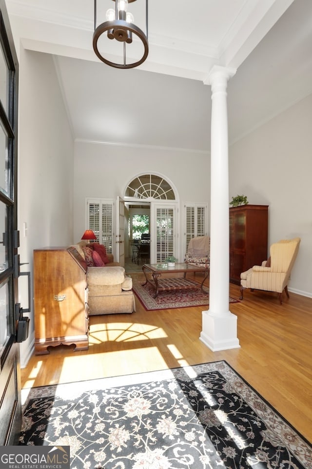 living area with a towering ceiling, hardwood / wood-style floors, ornate columns, and crown molding