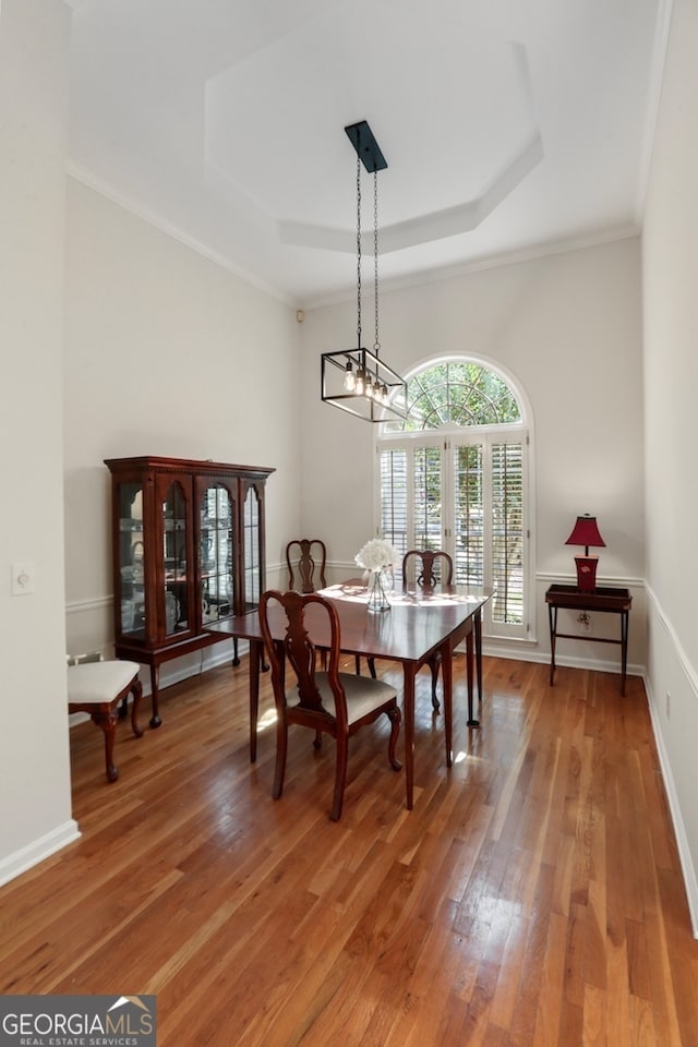 dining space featuring ornamental molding, a chandelier, wood-type flooring, and a raised ceiling