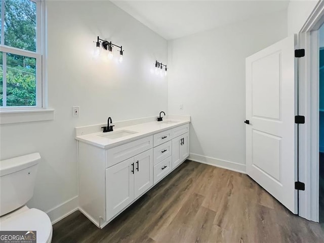 bathroom with wood finished floors, a sink, toilet, and double vanity