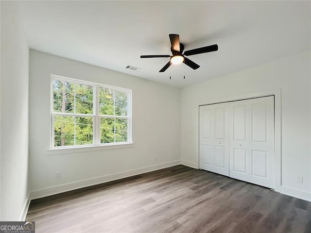 unfurnished bedroom with a closet, wood finished floors, visible vents, and baseboards