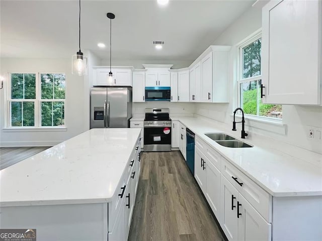 kitchen with appliances with stainless steel finishes, white cabinets, a kitchen island, and a sink