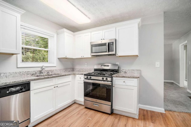 kitchen with light wood-type flooring, stainless steel appliances, a sink, and white cabinetry