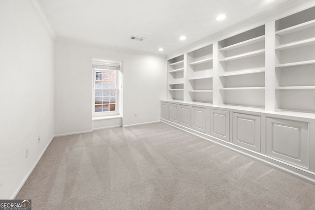 empty room featuring built in shelves, ornamental molding, and light colored carpet