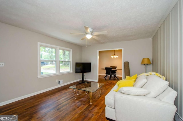 living room with ceiling fan with notable chandelier, a textured ceiling, and dark hardwood / wood-style floors