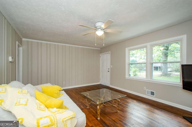 living room with a textured ceiling, crown molding, ceiling fan, and dark wood-type flooring