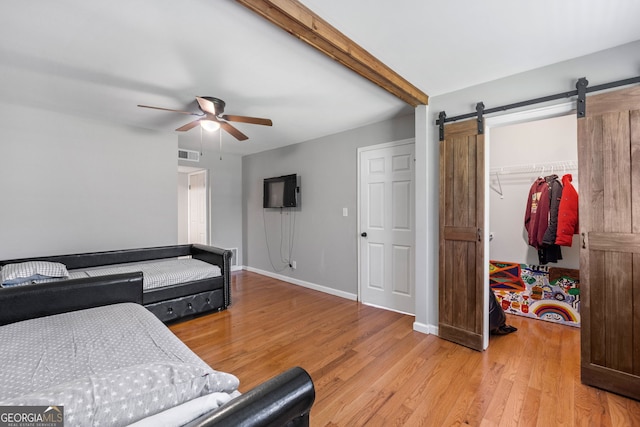 bedroom featuring a barn door, visible vents, a spacious closet, light wood-type flooring, and beam ceiling